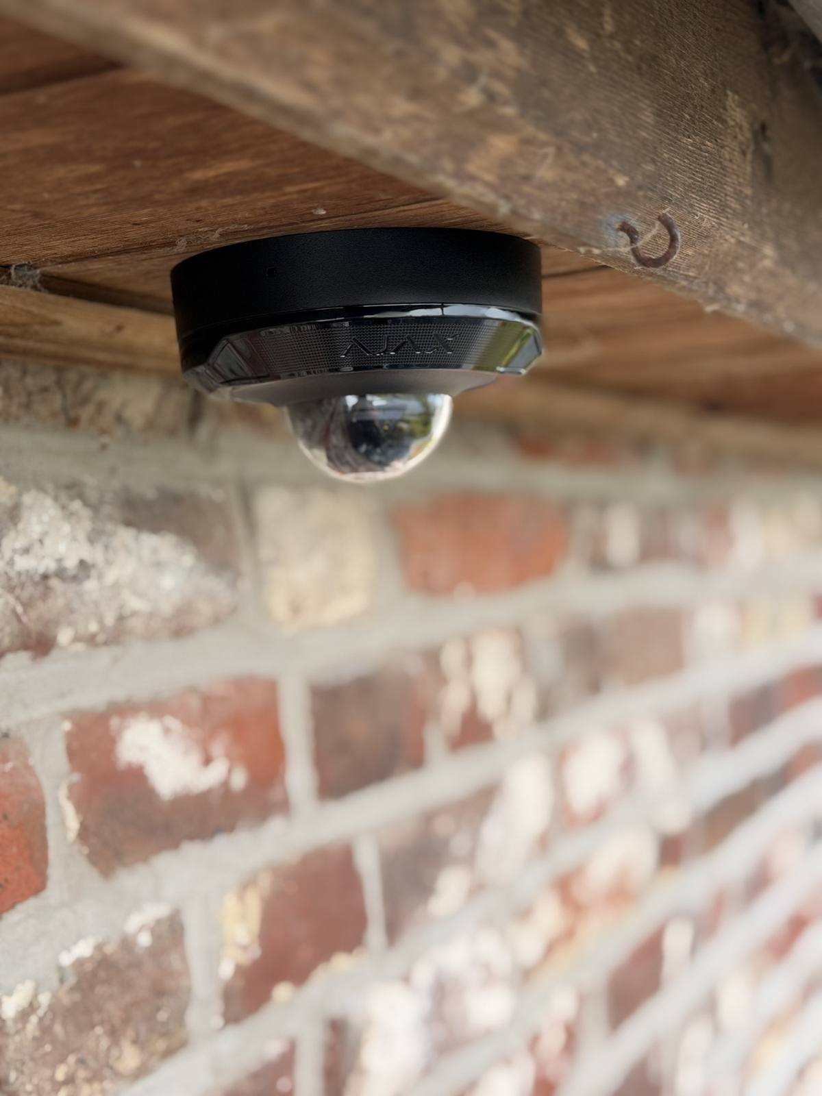 Ajax-camera onder een houten balk aan een bakstenen gevel.